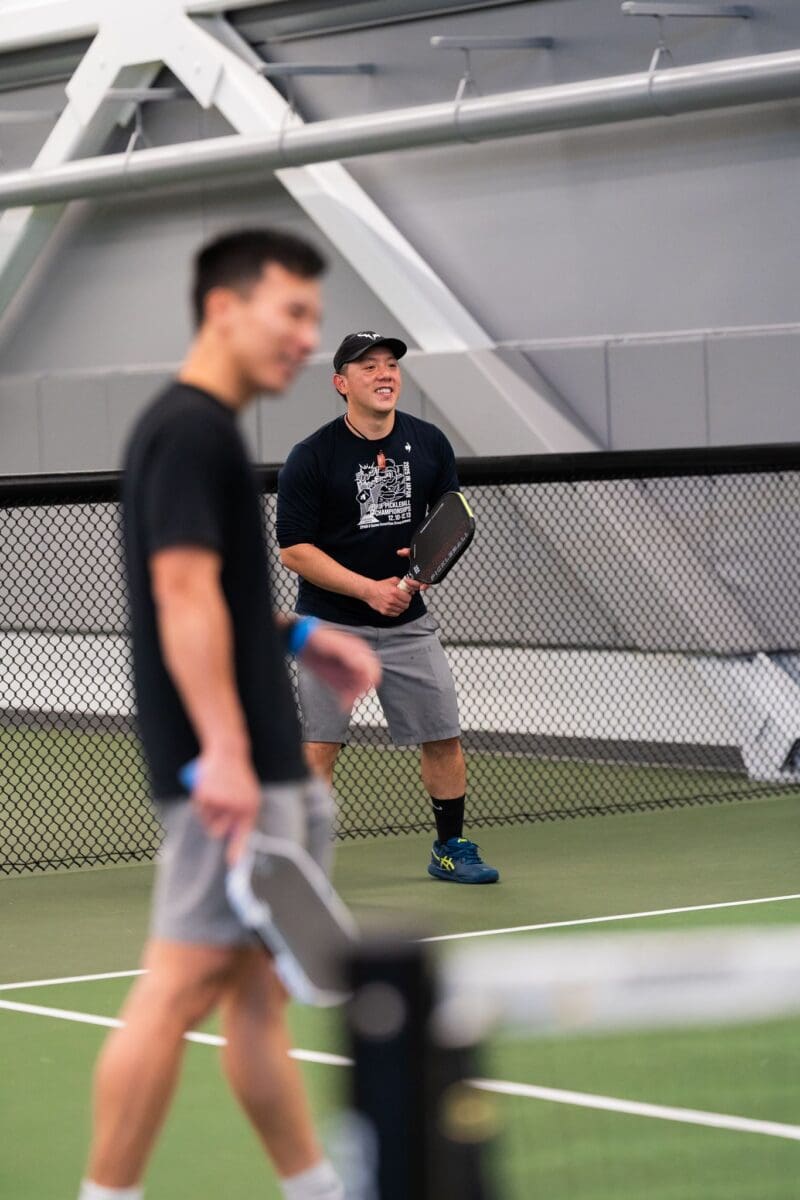 two young men laughing and playing pickleball